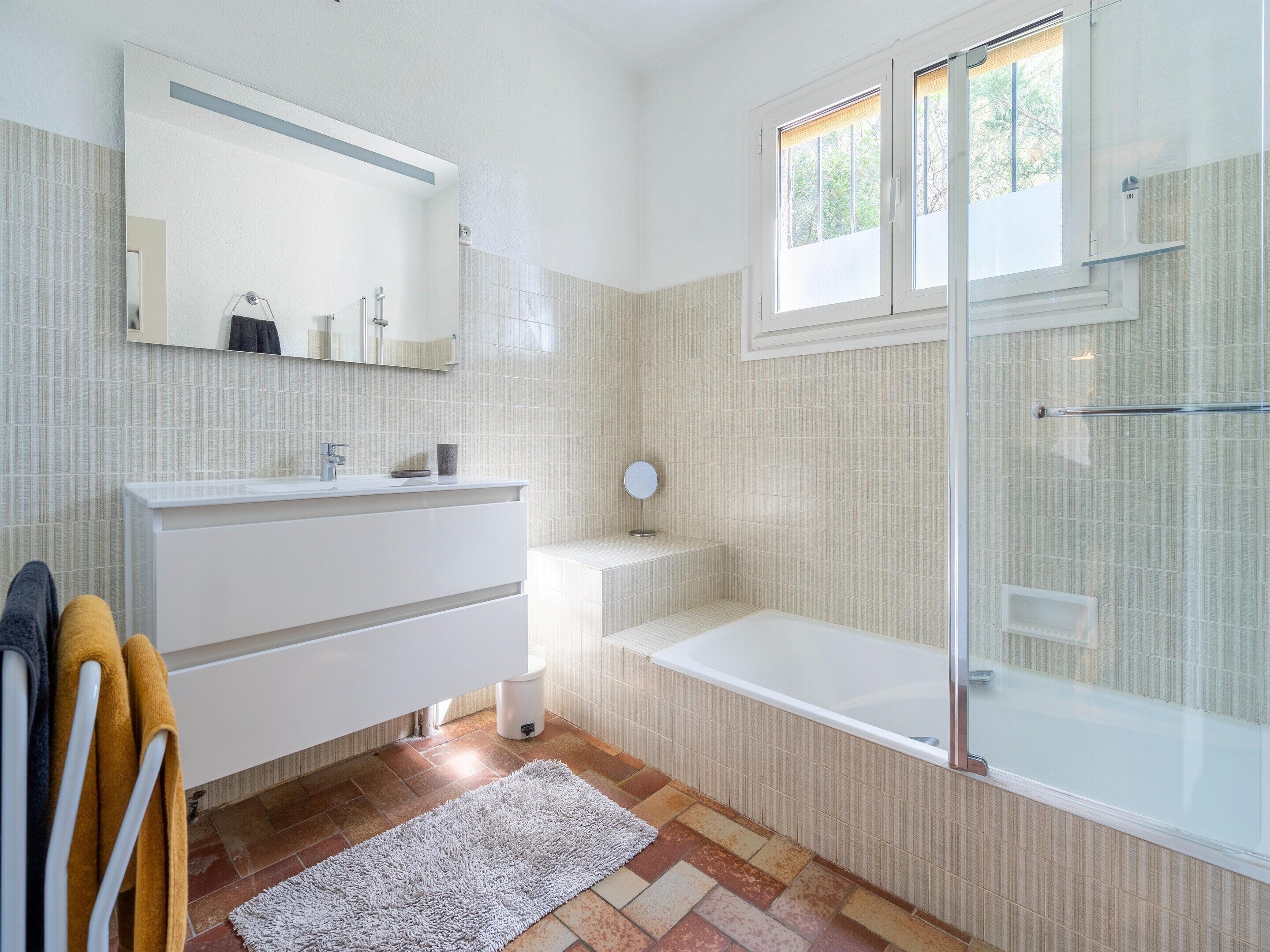 Une salle de bain moderne avec une douche en verre, un meuble-lavabo blanc et une grande fenêtre.