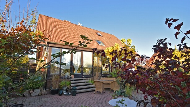 A house with a tiled roof, a glass door, and a brick patio with outdoor furniture.