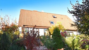 A house with a tiled roof, a visible satellite dish, and a garden with various plants and shrubs.