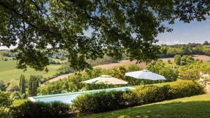 Un espace piscine agrémenté de parasols, entouré d’une végétation luxuriante et offrant une vue sur la campagne.
