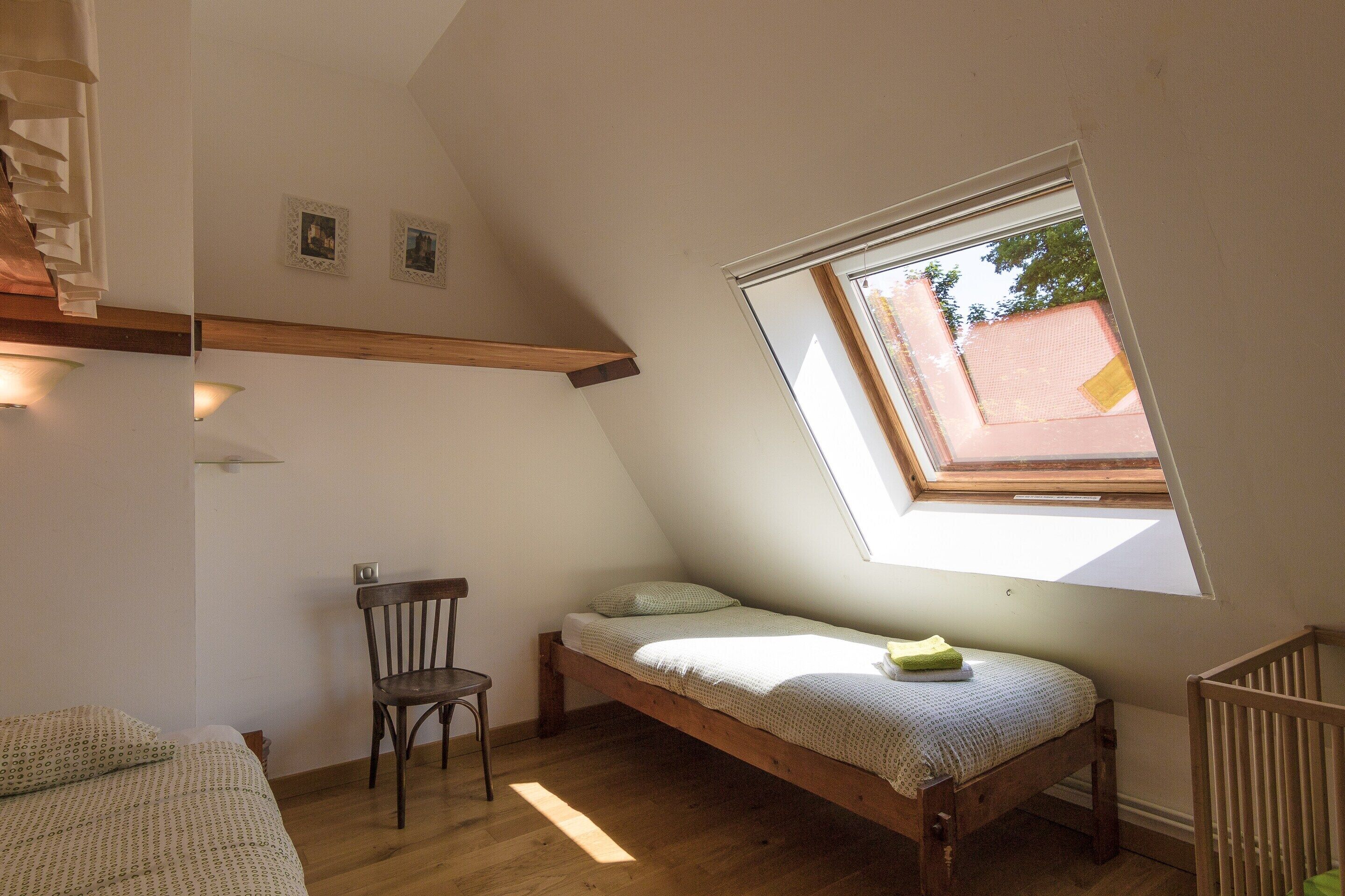 A room with a sloped ceiling, a single bed, a chair, and a window.