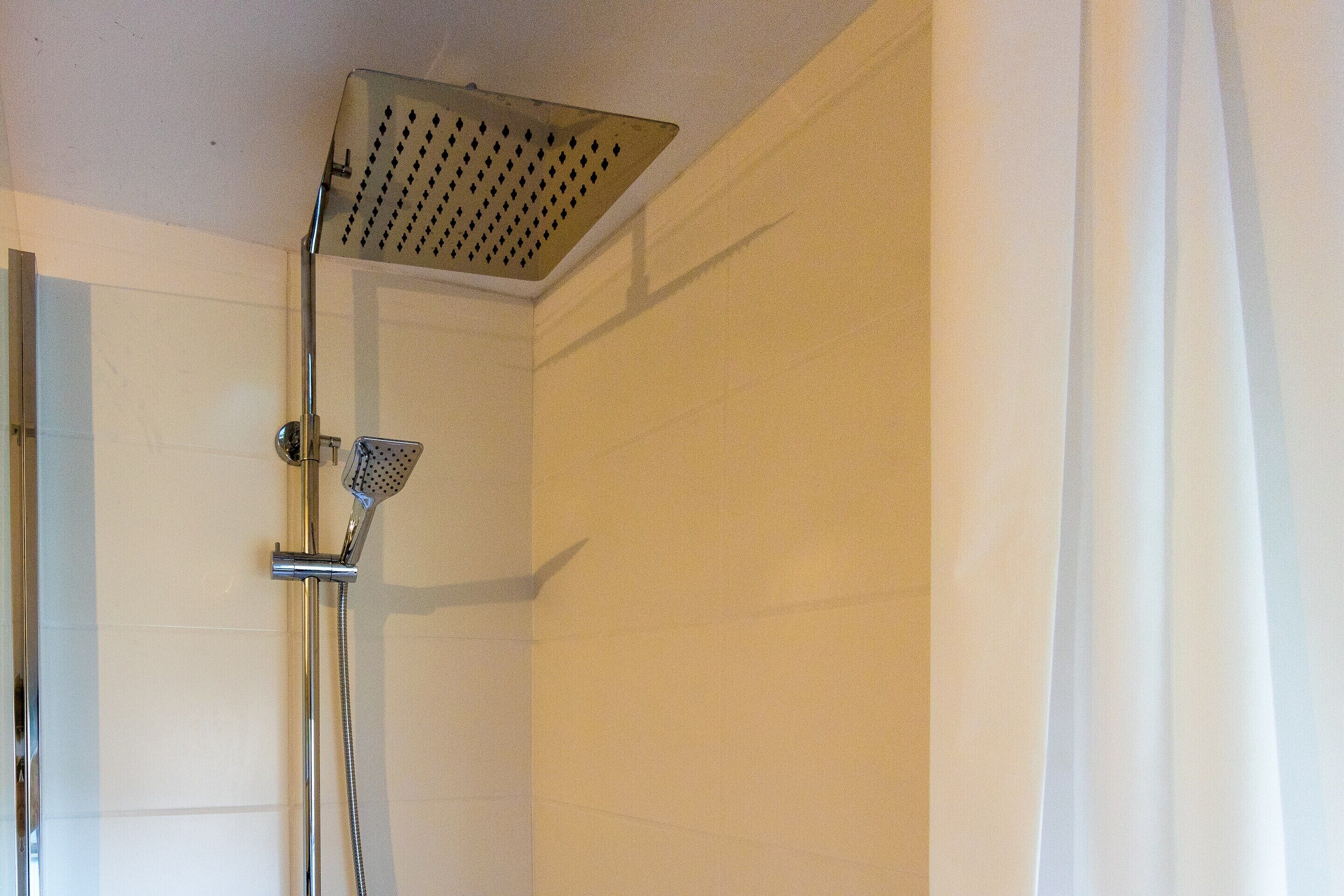 A shower with a handheld showerhead and a wall-mounted rain showerhead in a bathroom with white walls.