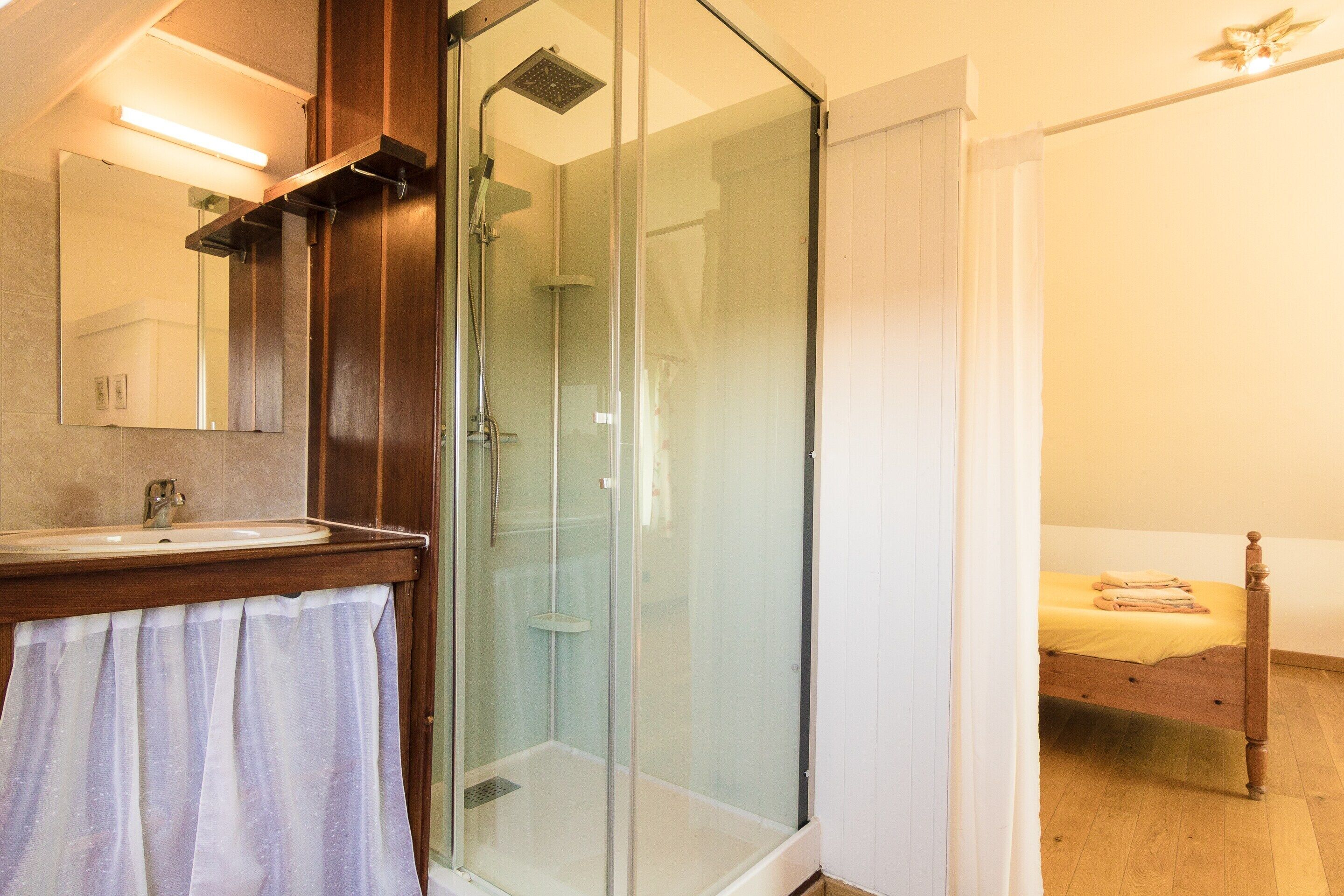 A bathroom with a glass shower enclosure, a sink, and a mirror.