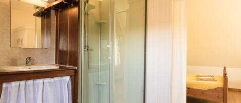 A bathroom with a glass shower enclosure, a sink, and a mirror.