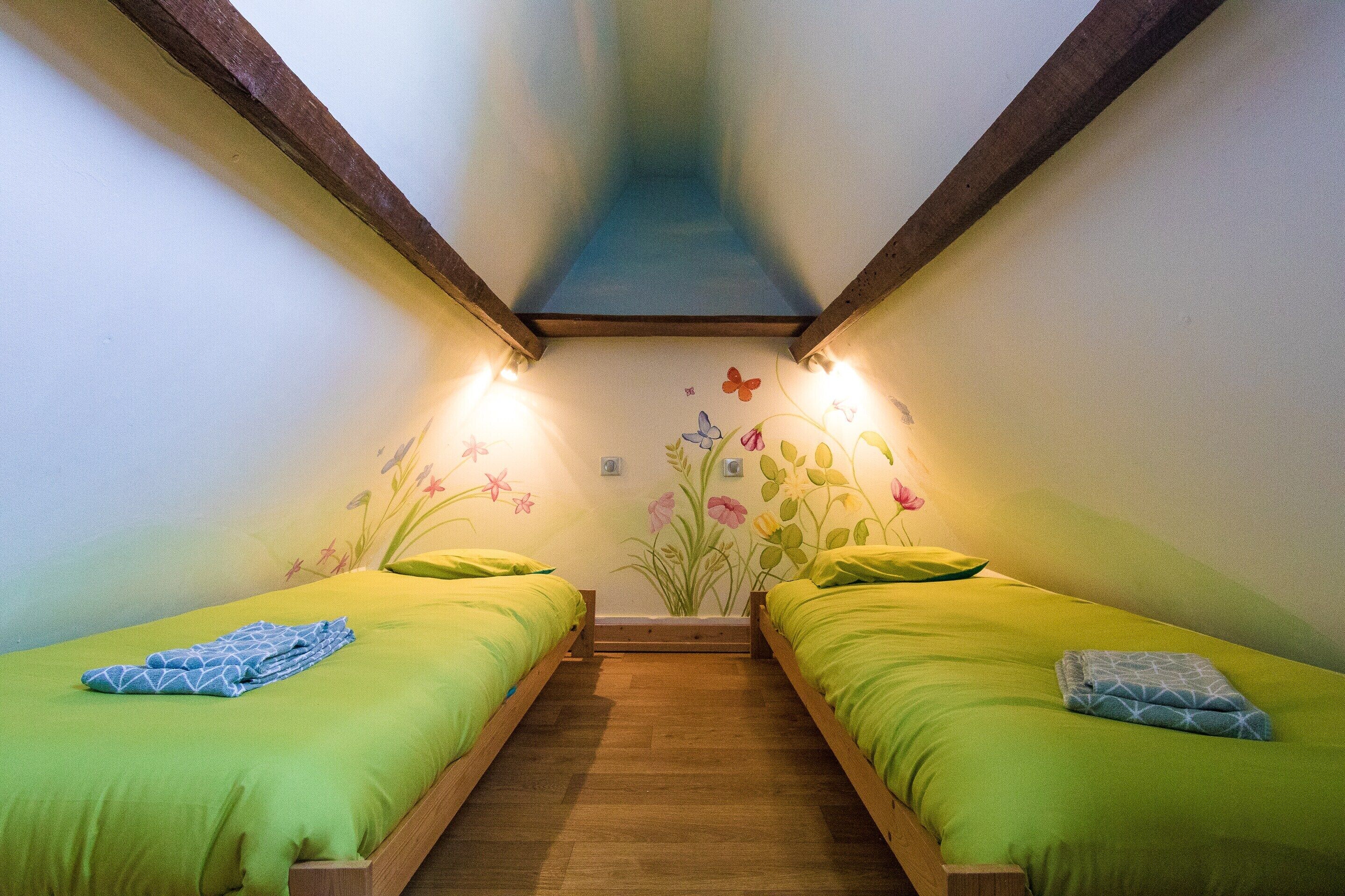 Une chambre avec deux lits, des poutres en bois au plafond et une fresque murale à motifs floraux.