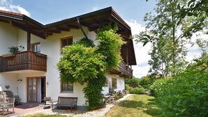 A two-story house with a balcony, a garden, and a wooden bench.