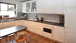 A modern kitchen with white cabinets, a black countertop, and a built-in oven. There are two wooden stools at a table, and a window provides natural light.