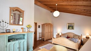 A bedroom with a wooden ceiling, a bed, a nightstand, a dresser, a chair, and a hanging light fixture.