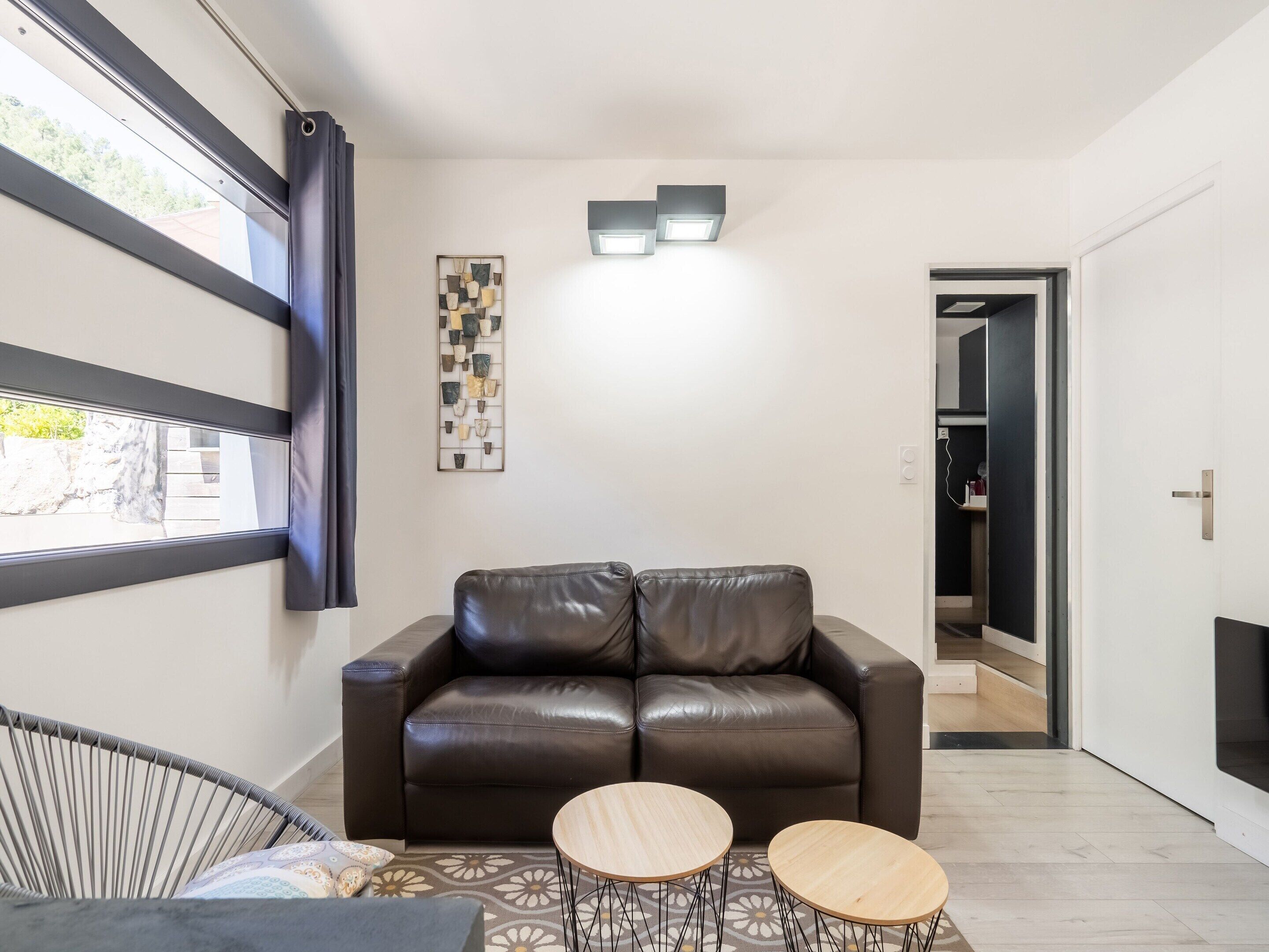 A modern living room with a leather sofa, two small round tables, a decorative wall piece, and a window with curtains.