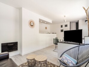 A modern living room with a flat-screen TV, a dining area with a glass table and chairs, a fireplace, and a kitchen area with a countertop and cabinets. - Elegant Villa With Private Pool (Les Vans)