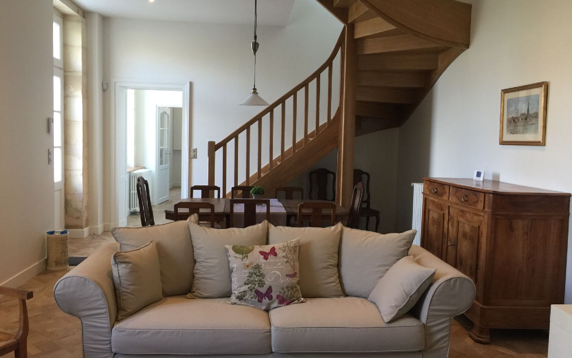 A living room with a sofa, wooden staircase, dining table, and chairs.