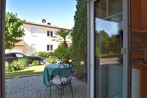 A patio with a table and chairs, a car parked outside, and a building with a tiled roof in the background. - Apartment Near the Bavarian Forest (Deggendorf)
