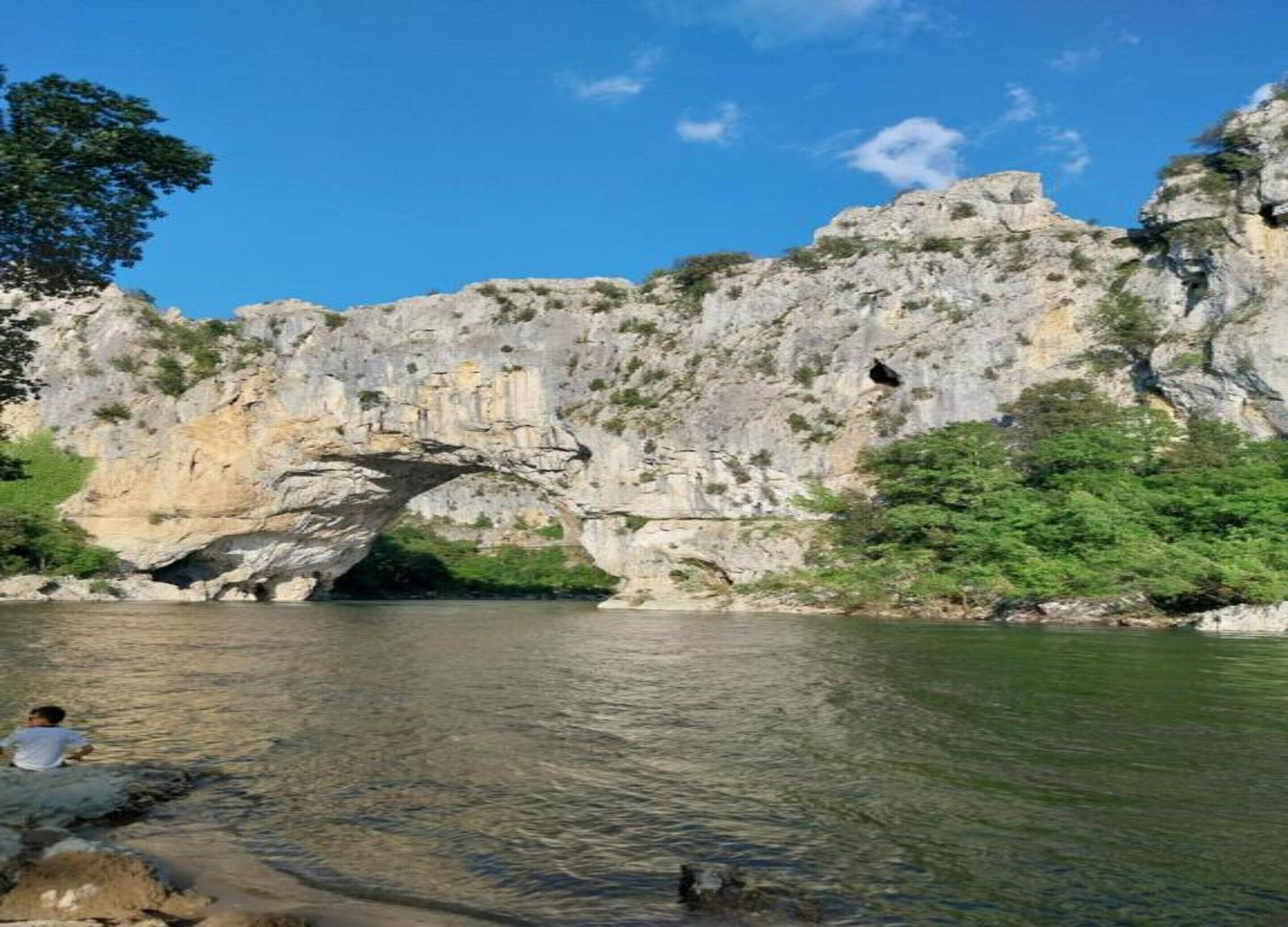 A natural rock formation with a cave-like opening and a river flowing through it.