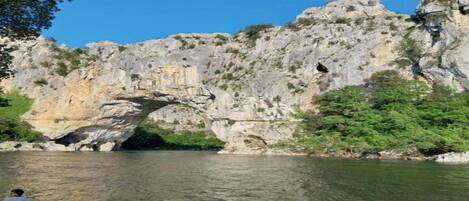 A natural rock formation with a cave-like opening and a river flowing through it.