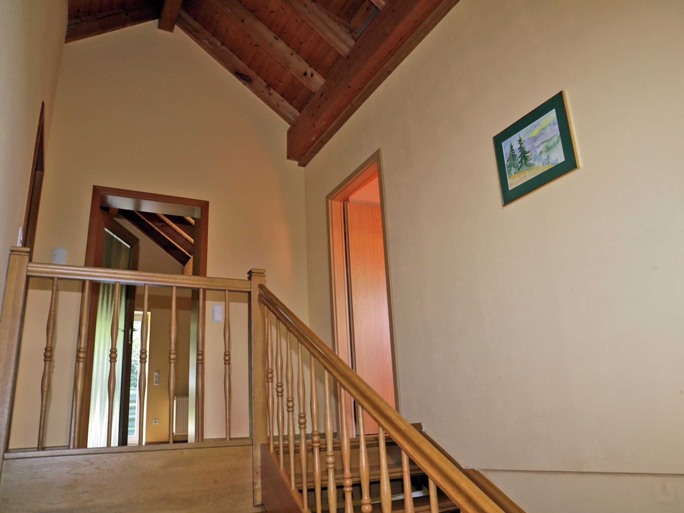 A wooden staircase with a handrail leading to a second-floor landing. A framed picture hangs on the wall above the staircase.