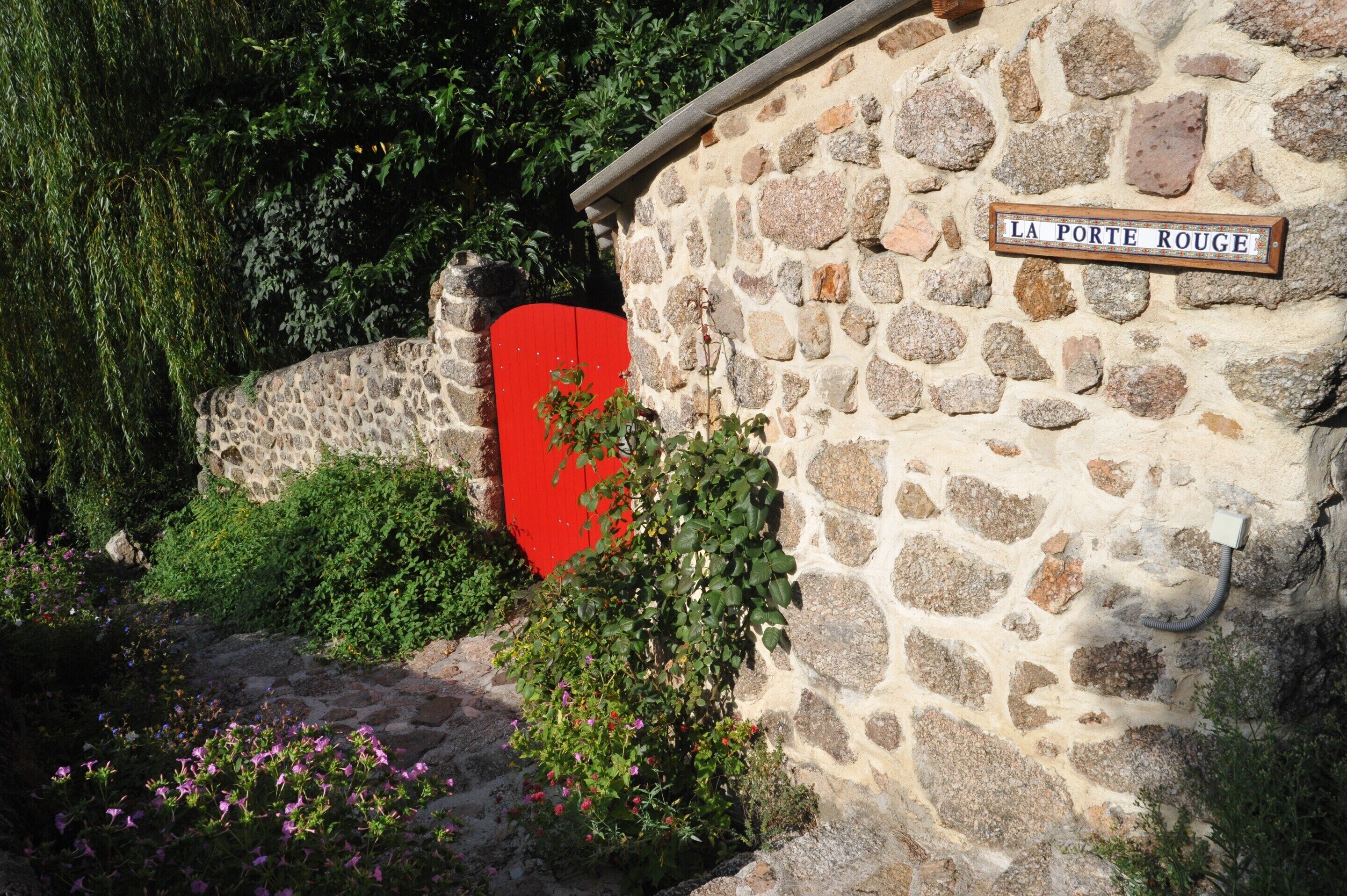 A stone wall with a red gate and a sign reading 'La Porte Rouge'.