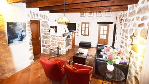 A stone-walled room with a fireplace, red chairs, a table with a vase of flowers, and a television. - Escape in Duniere-sur-eyrieux (Duniere-sur-Eyrieux)