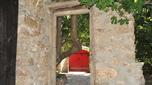 A stone archway leading to a red door, surrounded by greenery and a cobblestone path. - Escape in Duniere-sur-eyrieux (Duniere-sur-Eyrieux)