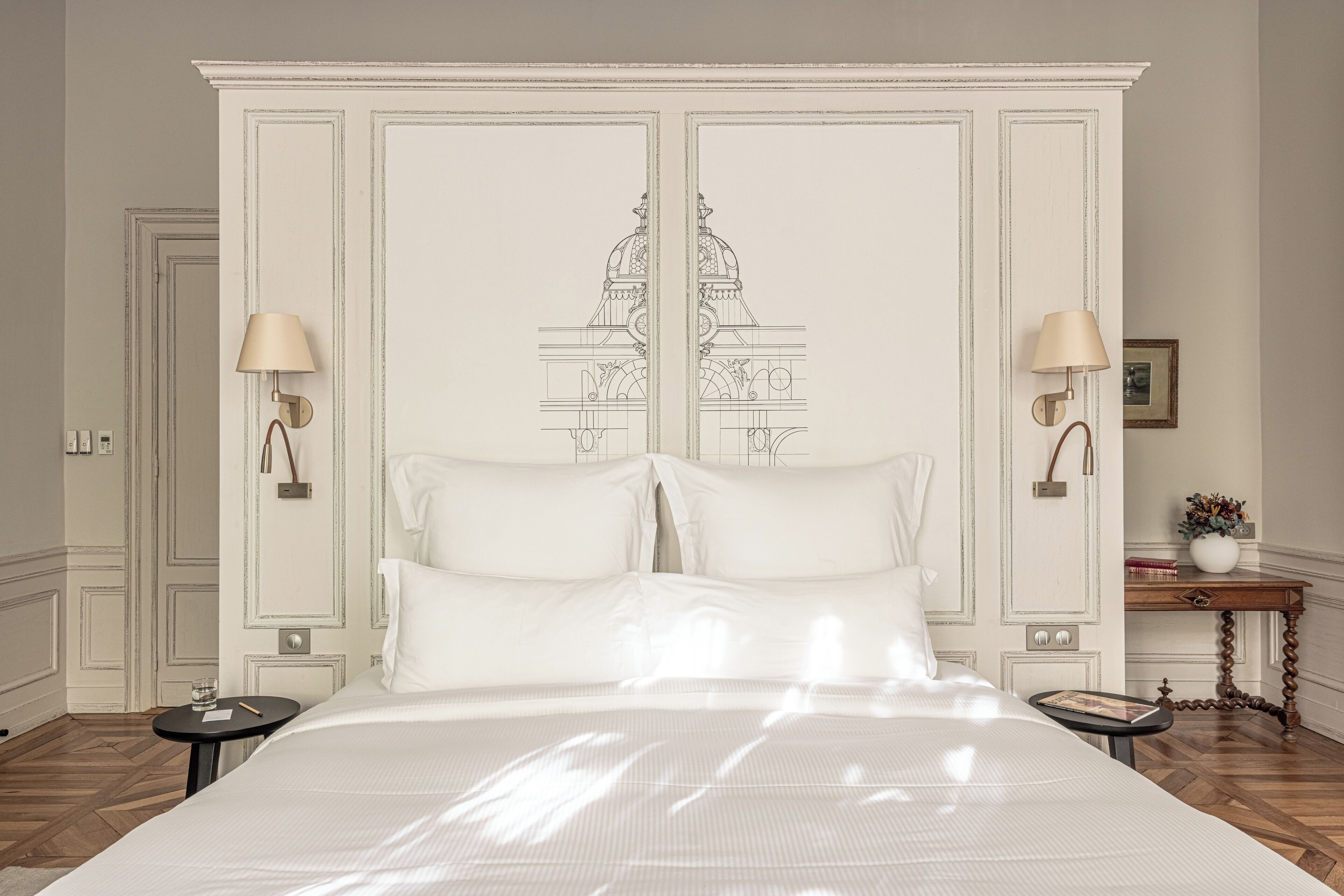 A bedroom with a large bed, two bedside tables, a nightstand, and a wall-mounted lamp.