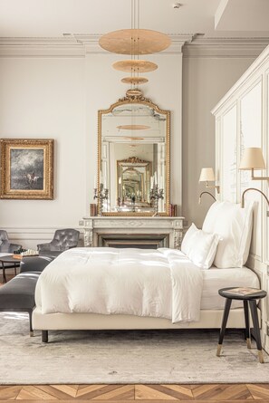 A bedroom with a large bed, a fireplace, a mirror, and a chandelier. - Villas Foch (Bordeaux)