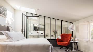 Una habitación de hotel moderna con una cama grande, un sillón rojo, una mesita con vasos y un espejo amplio.