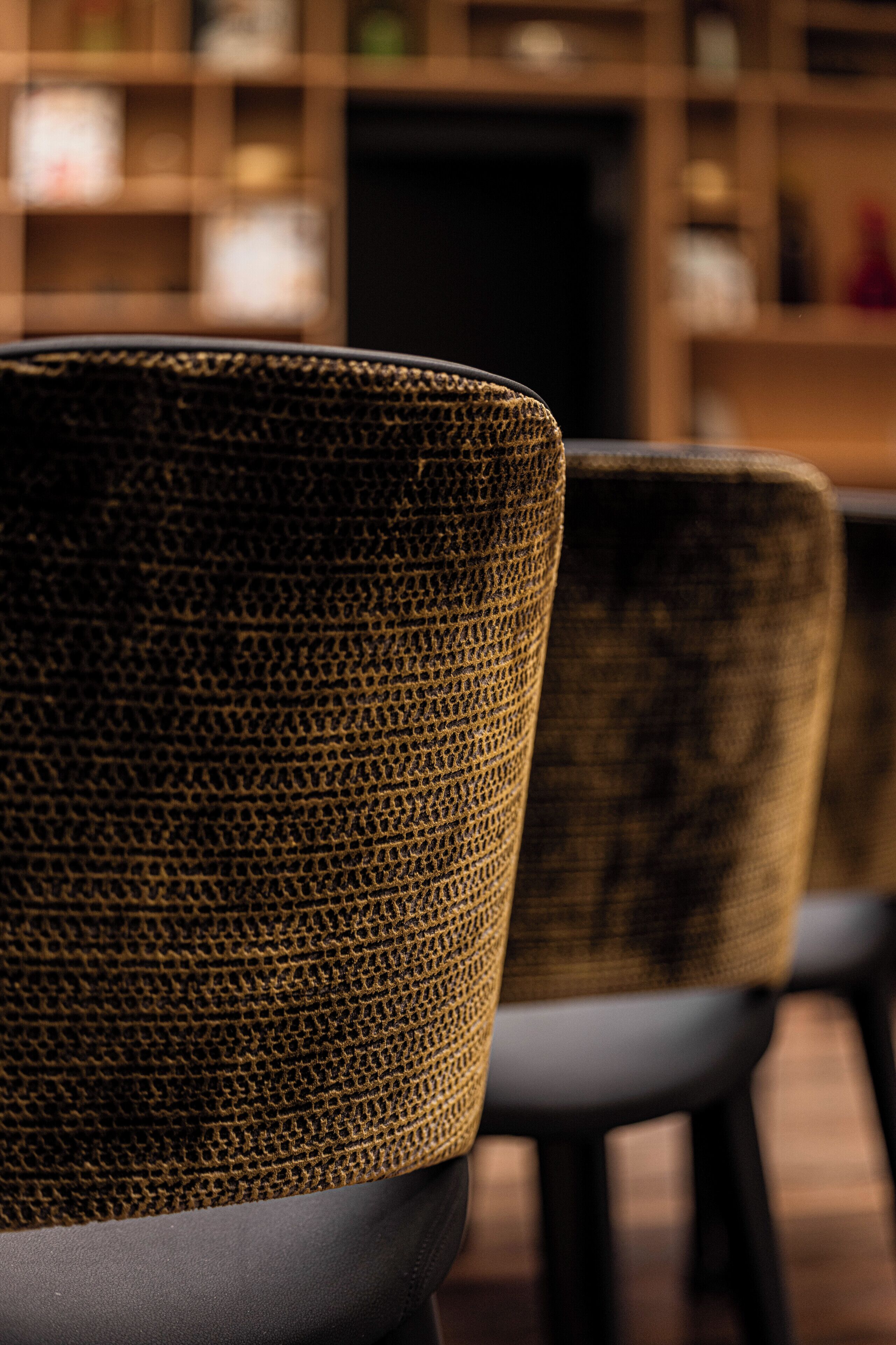 A close-up of a textured woven chair with a dark cushion, part of a seating arrangement in a room with a blurred background.