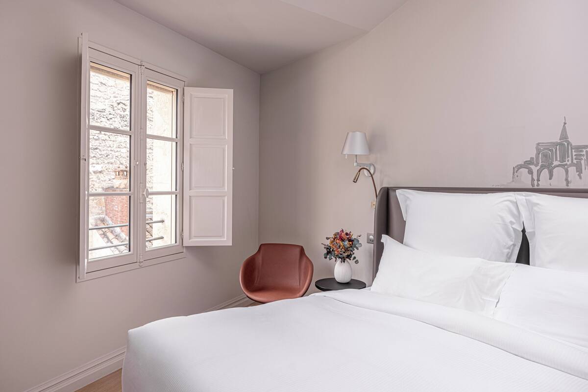 Quarto de hotel com cama, cadeira, luminária e parede com um mural.