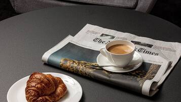 A round table with a newspaper, a cup of coffee, and a croissant.