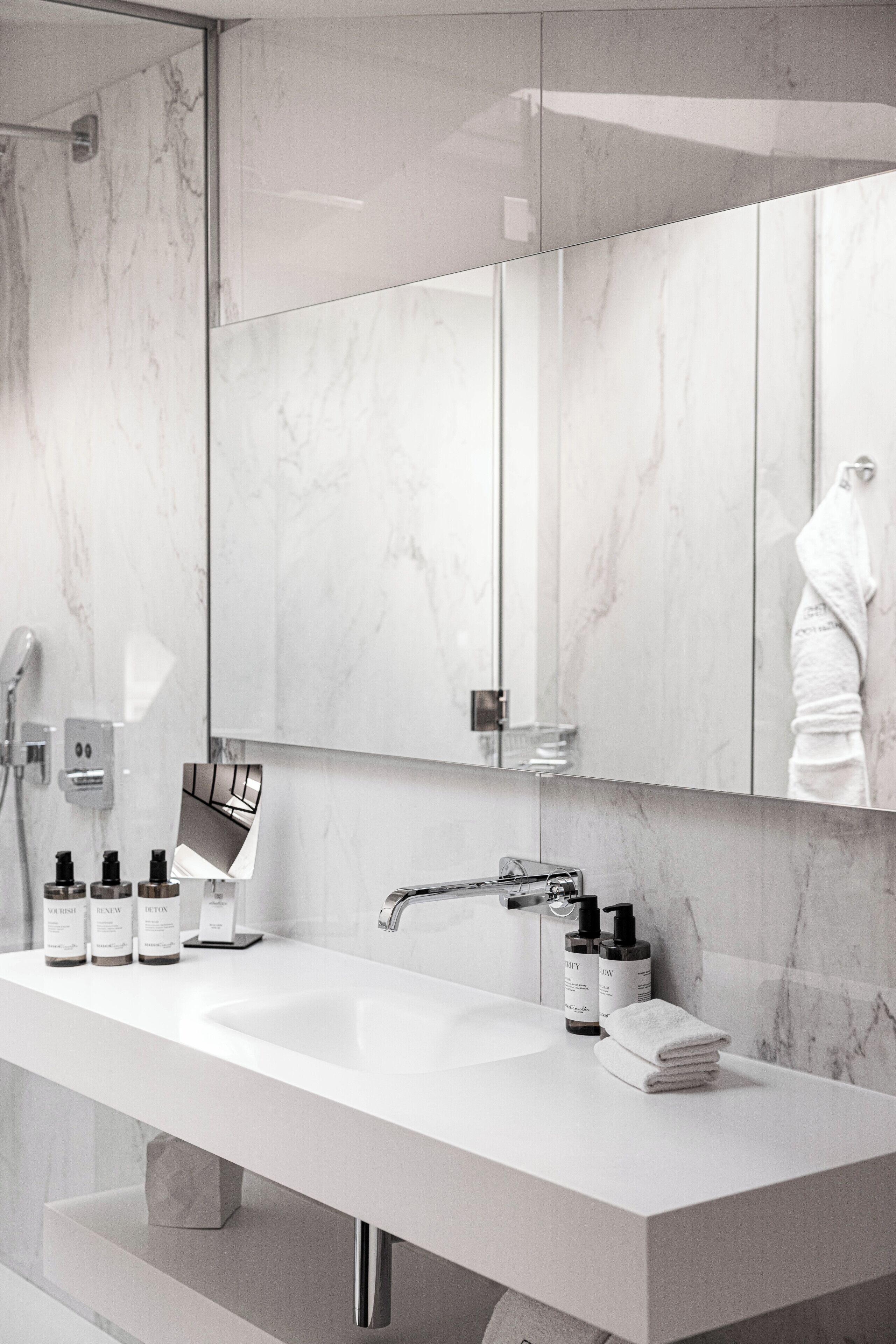 A modern bathroom with a white sink, marble walls, a large mirror, and toiletries.