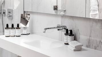 A modern bathroom with a white sink, marble walls, a large mirror, and toiletries.