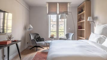 A hotel room with a bed, a desk, a chair, a bookshelf, and a window with a view.