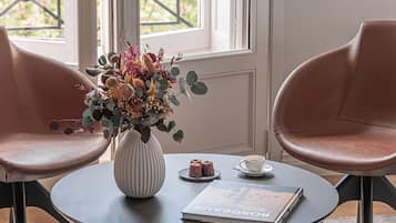 Una habitación con una mesa redonda, dos sillas, un jarrón con flores, un libro y una ventana con vistas a la vegetación.