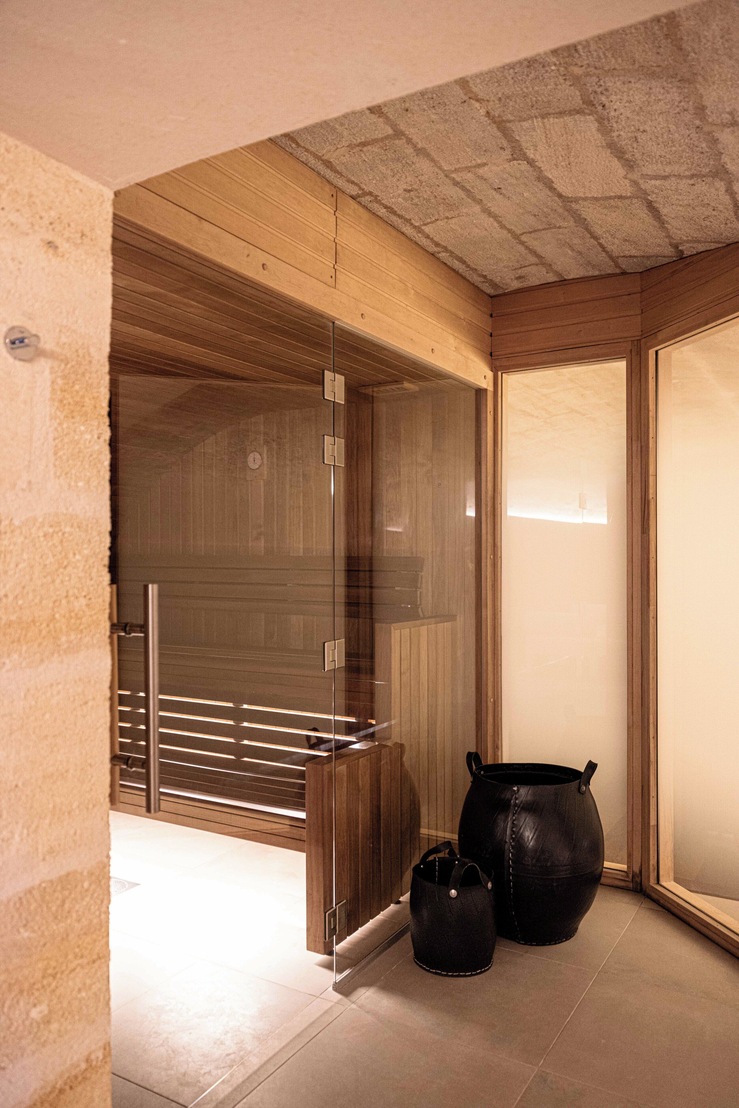 A modern interior with a wooden ceiling, a glass door leading to a sauna area, and two black leather bags on the floor.
