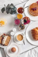Desayuno con panqueques, huevos, pastelería y diferentes opciones para untar en platos.