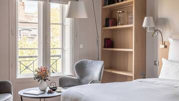 Habitación de hotel con cama, escritorio con lámpara, silla, estantería y vistas al exterior.