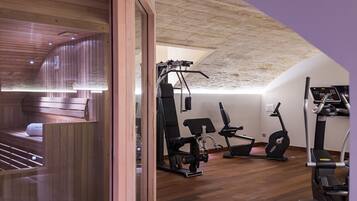 A gym with wooden flooring, exercise equipment, and a sauna area.