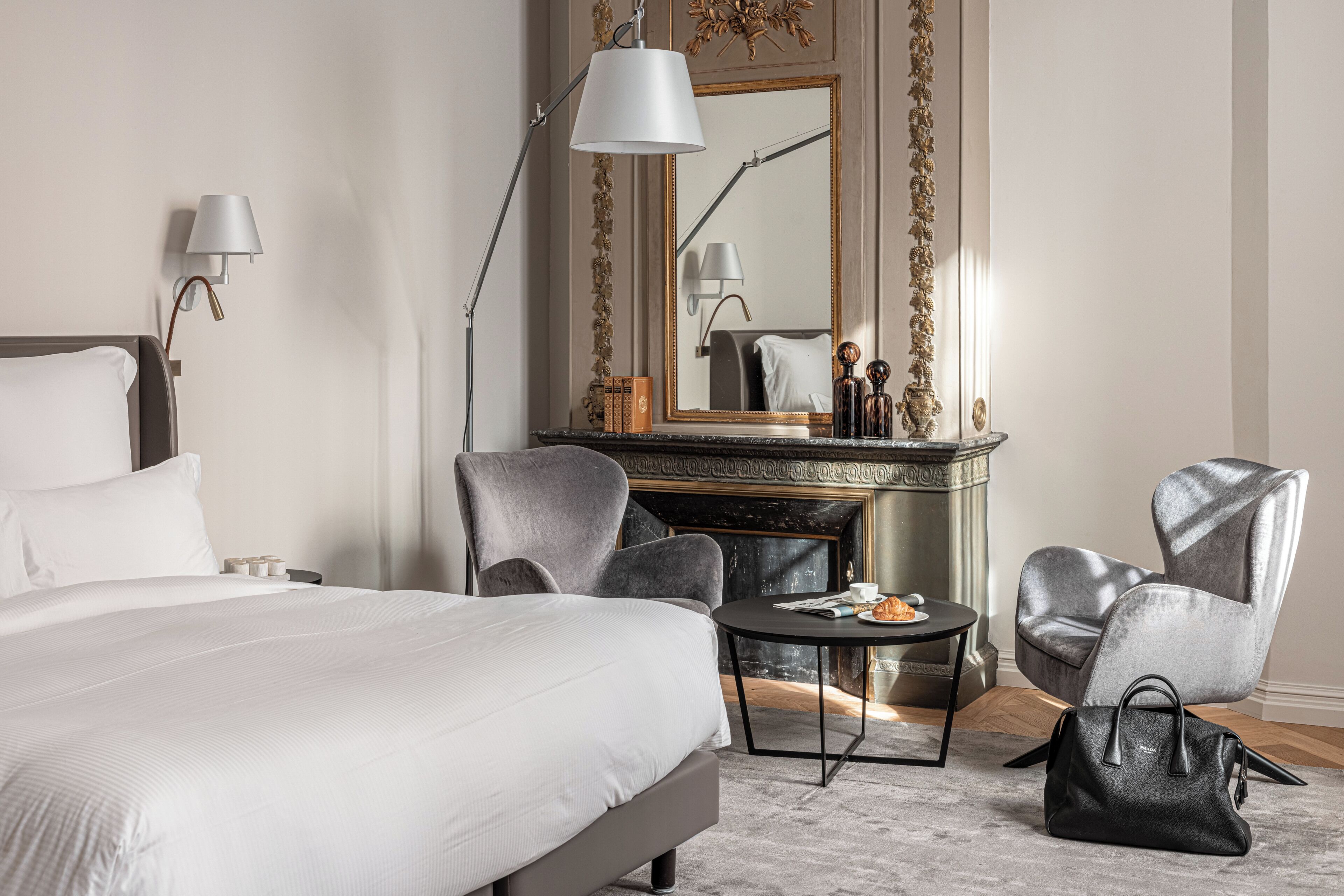 A hotel room with a bed, two armchairs, a round table, a fireplace, and a mirror.