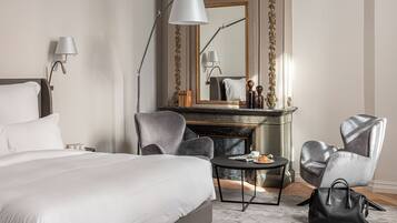 A hotel room with a bed, two armchairs, a round table, a fireplace, and a mirror.