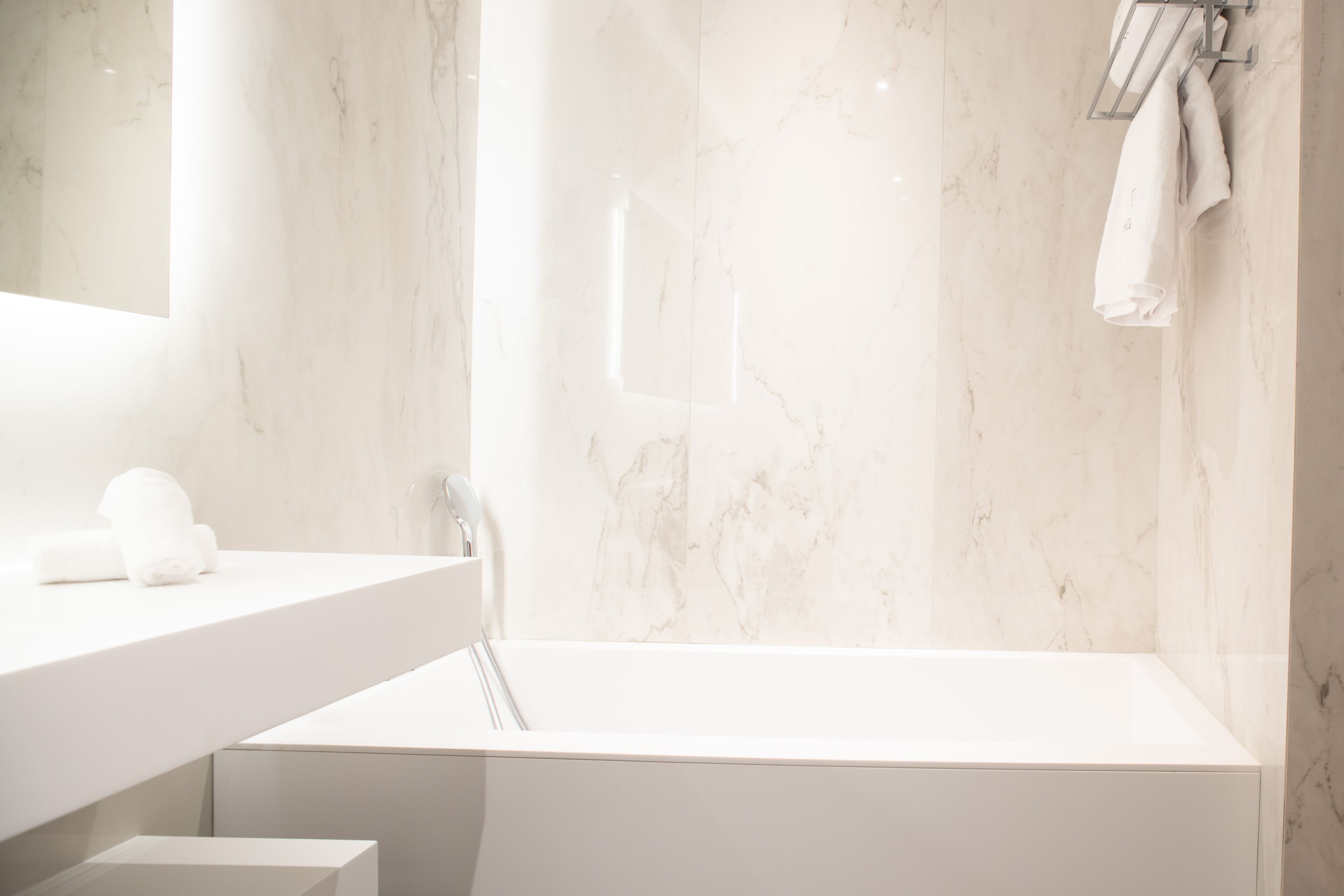 Un baño moderno con pared de mármol, lavamanos blanco y bañera.