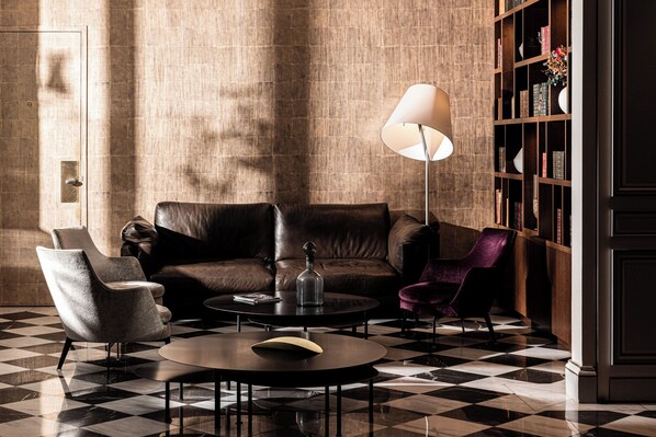 A room with a checkered floor, a leather sofa, a purple armchair, a round table, and a bookshelf. - Villas Foch (Bordeaux)