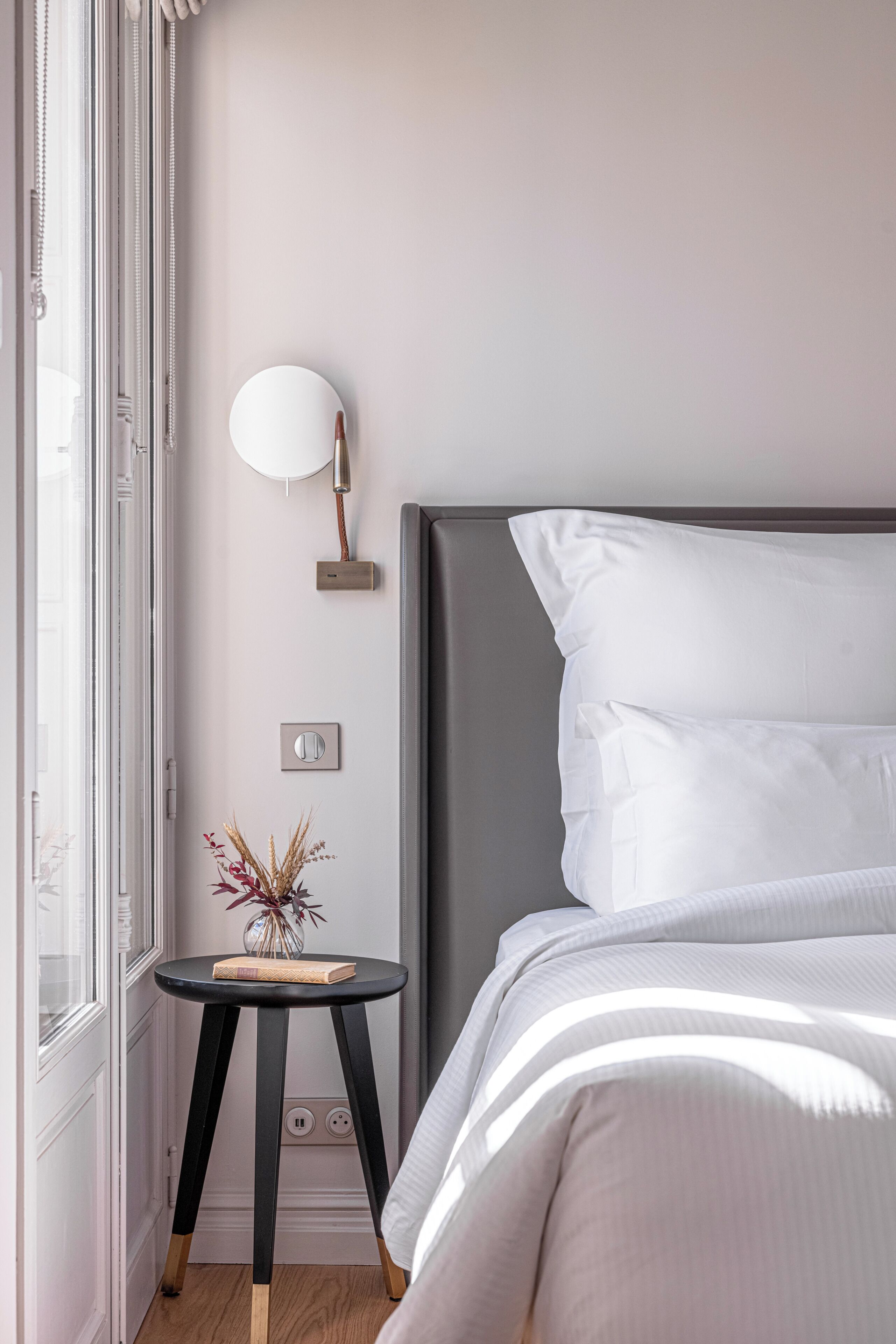 A bedroom with a bed, bedside lamp, and a small table with a vase and book.