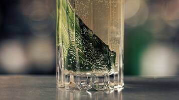 Un vaso transparente con una guarnición verde sobre una superficie reflectante.