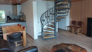 Ett modernt kök med ett matbord och stolar i trä, en svart lädersoffa och en spiraltrappa.