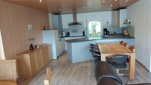 Ett modernt kök med en central köksö, träskåp och en matplats med ett träbord och stolar.