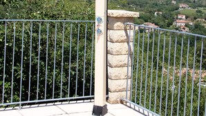 A balcony with a stone wall and metal railing overlooking a hilly landscape with houses. - Quiet Holiday Home in Les Vans With Pool (Les Vans)