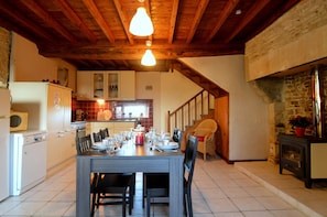 Un coin repas avec une table en bois dressée pour quatre personnes, une cuisine en arrière-plan et une cheminée en pierre.