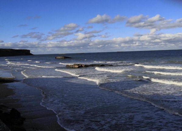 Une plage avec des vagues, une falaise et un ciel dégagé.