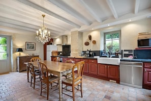 A kitchen with a dining table, chairs, a chandelier, and a large window. - Manor in Normandy With Spa and Pool (Ponts sur Seulles)