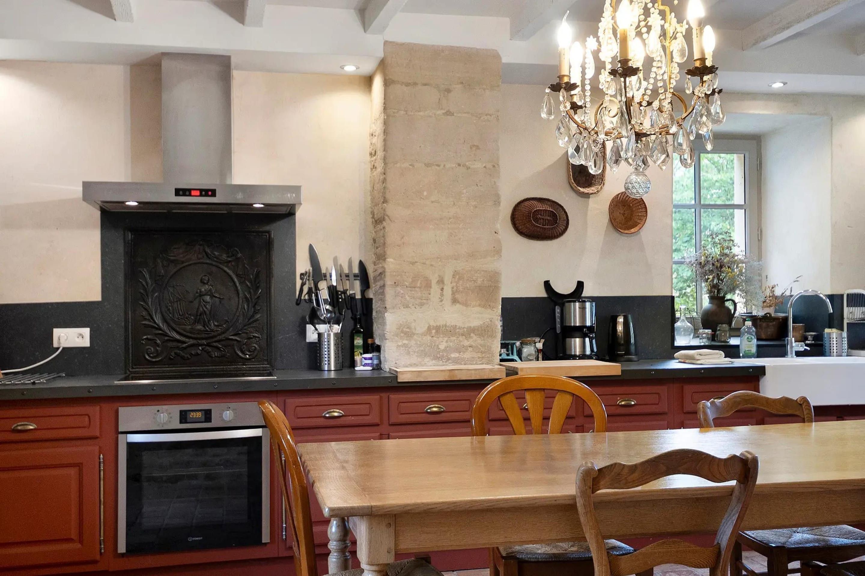 A kitchen with a central island, a chandelier, and a dining area with wooden chairs.