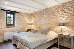 A bedroom with a stone wall, a double bed, two bedside tables with lamps, and a window with a view. - Manor in Normandy With Spa and Pool (Ponts sur Seulles)